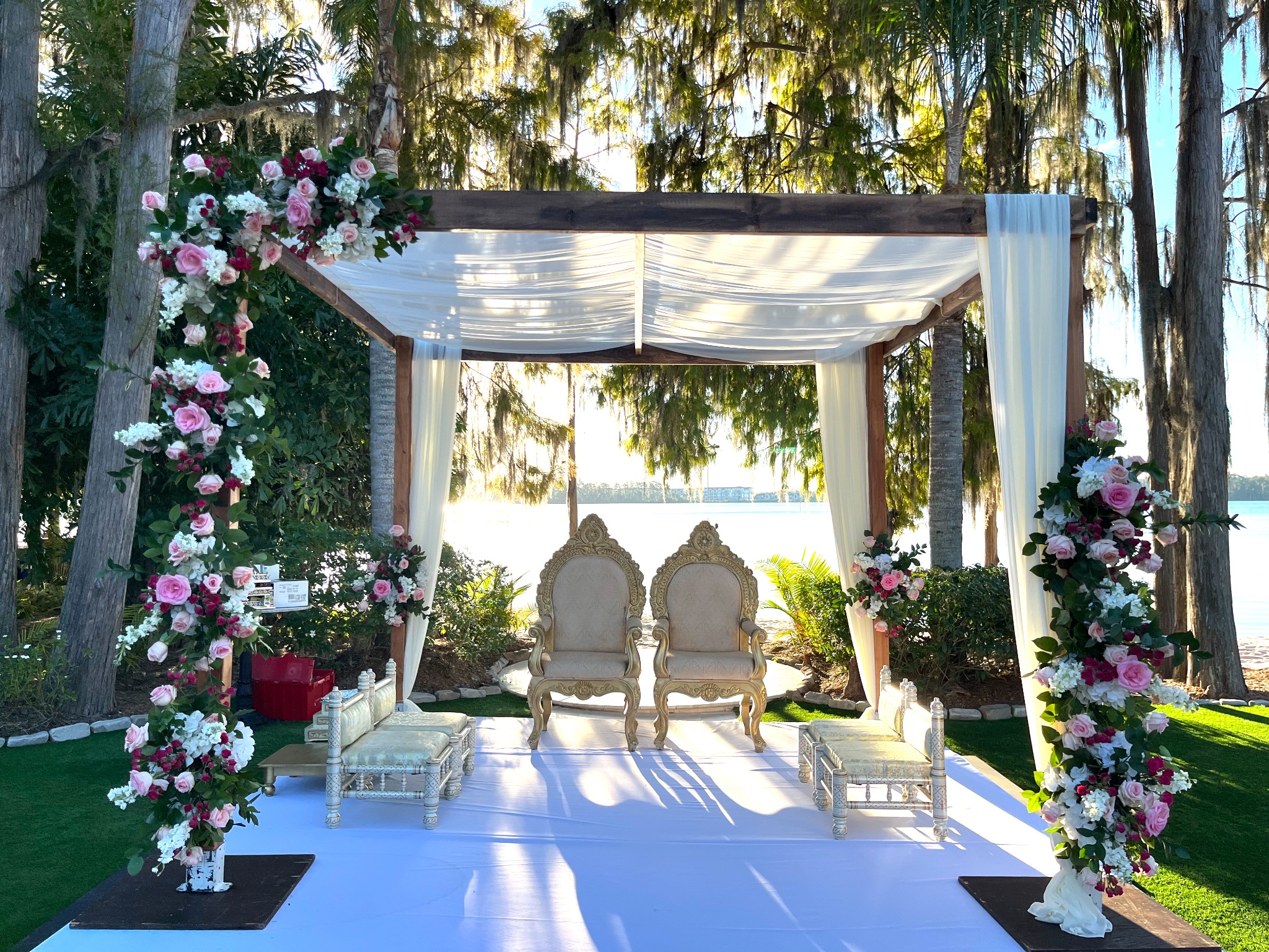 Rustic dark-wood lakeside mandap with pink, burgundy, and white florals